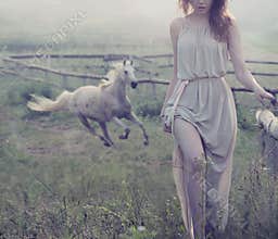 Delicate brunette posing with horse in the background
