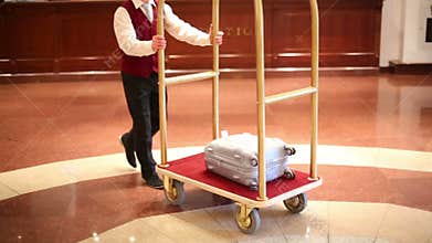 Receptionist in red vest carries suitcase of guest