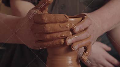 The hands of man potter support a spinning jug and daub it with a layer of clay. A child in the back background observes