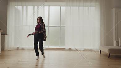A woman is joyfully dancing in a cozy living room with natural light coming through the window