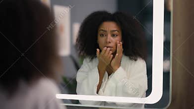 Worried African American woman looking in mirror feeling stressed facial wrinkles acne blackheads problem frustrated