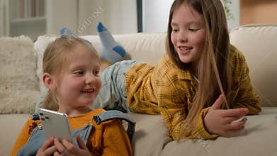 Internet addicted smiling carefree Caucasian girls children little kids show screen use social media app on mobile