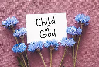 Child of God - christian text on card with blue cornflower flowers bouquet on dark purple background, religion concept