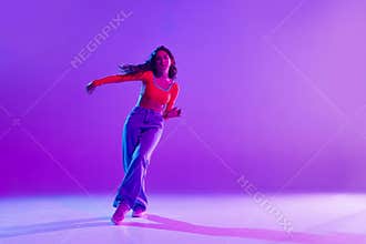Burst of energy. Stylish young girl in casual clothes, in motion, dynamically dancing hip hop against multicolored