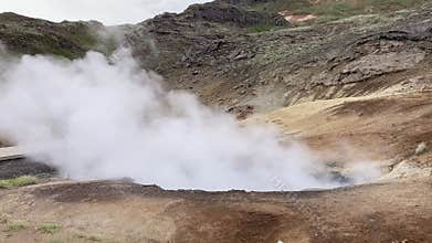 mudpot in Iceland with smoke blowing in the wind and black mud jumping up in the cloud of smoke
