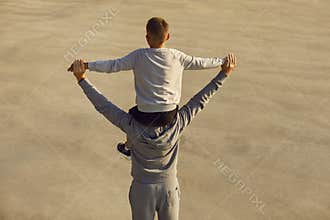 Back view of child boy in sportswear sitting on fathers shoulders after sport workout outdoors