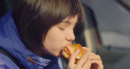 Close-up footage of a teenager girl eating burger while sitting in a car.