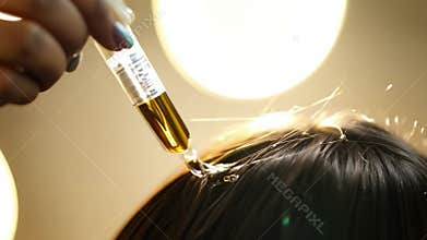 Close-up of a hair treatment process with oil being applied to the scalp, highlighting beauty and hair care techniques