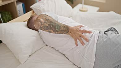 Handsome young man in pain, suffering from a back injury, lying in bed, touching his aching spinal column, a look of hurt