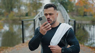 Sportive Caucasian Man Walking in the Park with Towel on his Shoulder, Recording a Voice Message to Share his Sport