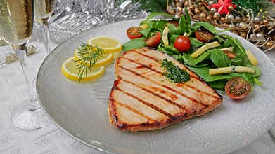 Grilled swordfish steak with fresh salad, tomatoes and cheese on a plate rotating. Christmas New Year decoration.