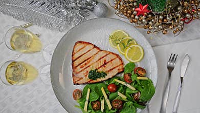 Grilled swordfish steak with fresh salad, tomatoes and cheese on a plate rotating. Christmas New Year decoration.