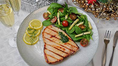 Grilled swordfish steak with fresh salad, tomatoes and cheese on a plate rotating. Christmas New Year decoration.