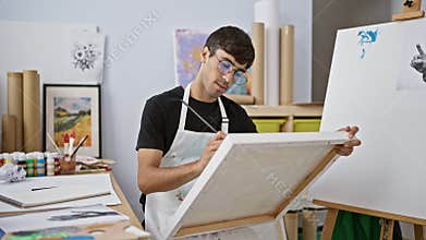 Attractive young hispanic man, an aspiring artist, lost in thought whilst drawing in a college art studio, palette in hand and