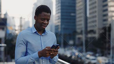 Handsome Employee Standing in the Business District and Texting with Clients. African American Young Businessman