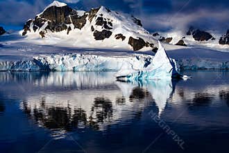 Winter landscape, first sun light on snowcapped mountains, reflections in water, small iceberg, Lemaire Channel near Paradise Bay