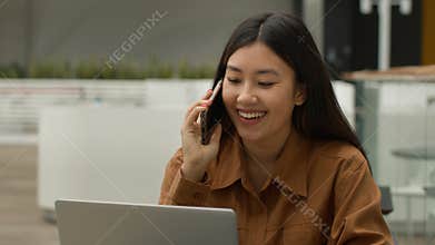 Asian businesswoman work multitask use laptop talk mobile phone solve online project with client in cafe smiling