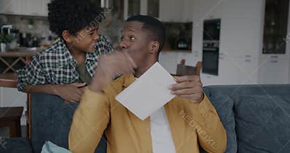 Happy African American man getting I love dad gift card from kid on father's day in kitchen at home