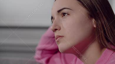 A pretty european or american young lady with a thoughtful sad gaze downcasts eyes and looks into the distance. A girl