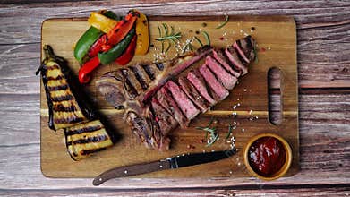 T- bone beef steak grilled sliced with grilled vegetables on wooden board. Top view