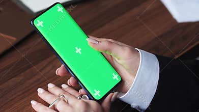 Woman using greenscreen phone in a busy office close up. The girl is using an app on a smartphone. Concept of chroma key