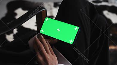 Woman using smartphone watching green screen on mobile phone in horizontal orientation person relaxing at home enjoying
