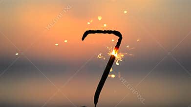 Sparkler in shape of number seven 7 burning against backdrop sea waves at dusk