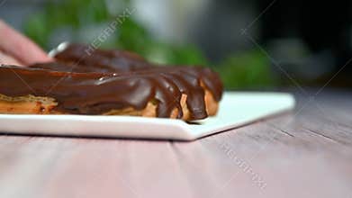 French dessert eclair with dark chocolate glaze. Woman putting baked French eclairs on a plate