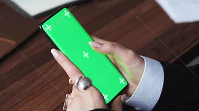 Women using smartphone with green background, scrolling on mobile phone green screen, close-up on hands. Concept of