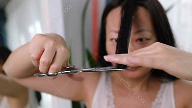 Young adult authentic asian woman self cutting bangs haircut with scissors.