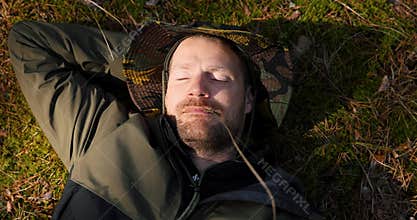 man sleeping and relaxing on green forest moss with blade of grass in mouth. nature escape and tranquility. stress relief