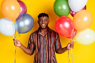 Photo of nice young man hold balloons wear shirt isolated on yellow color background
