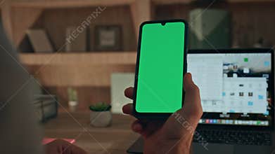 Online worker browsing greenscreen cellphone application at workplace close up.