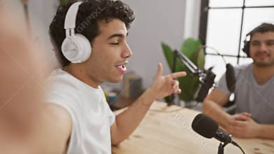 Two men podcasting in an indoor studio set with microphones and headphones, engaging in a discussion