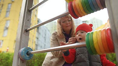 Slow motion. A little boy moves colorful wooden pucks on a large abacus while standing outdoors on a spring day at a