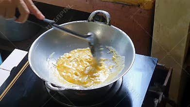 Stirring beaten eggs or whisked egg in the frying pan on the lit stove with a spatula, just like making a scrambled egg.