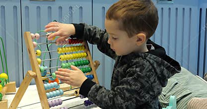 Curious preschooler boy moves bright wooden beads on abacus