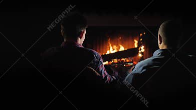 Two handsome men rest by the fireplace, slowly drinking brandy