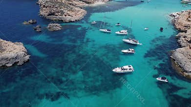 Boats floating in the crystal clear turquoise sea water. Blue lagoon, Comino, Maltese Islands. Aerial establishing view