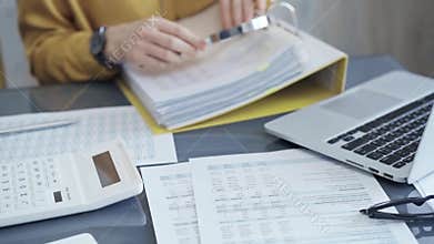 Female auditor in business attire inspecting financial reports with magnifying glass, surrounded by documents and a