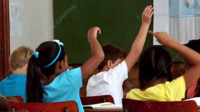 Young pupils raising hands during lesson in classroom