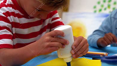 Cute little boy using glue in classroom
