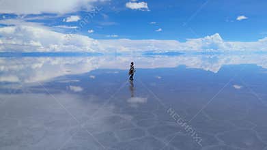 A solitary figure traverses the expansive Salar de Uyuni in Bolivia, captured under a clear midday sky
