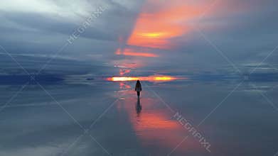 A solitary figure walks across the expansive salt flats of Bolivia during a breathtaking sunset