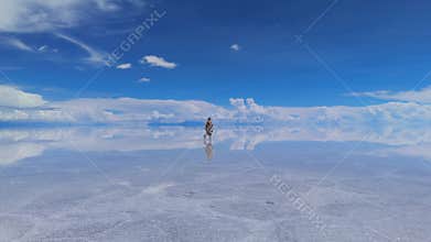 A woman walks across the expansive Salar de Uyuni salt flats in Bolivia, her reflection mirrored perfectly in the shallow water