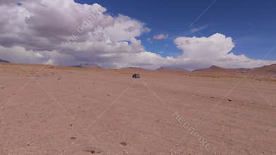 A solitary car traverses the expansive salt flats of Bolivia under a partly cloudy sky