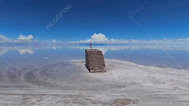 A woman standing on a brick staircase in the middle of a vast salt flat in Bolivia, with a stunning reflection of the sky on