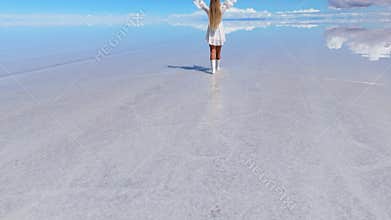 A woman walks across the expansive Salar de Uyuni salt flats in Bolivia under a clear blue sky