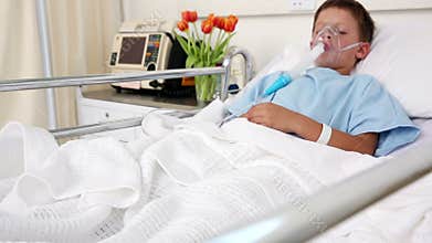 Little sick boy sleeping in bed with oxygen mask