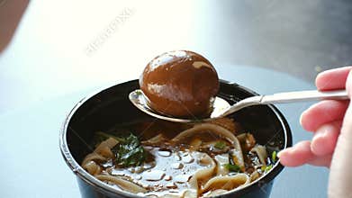 Hand lifting a marinated egg from ramen soup